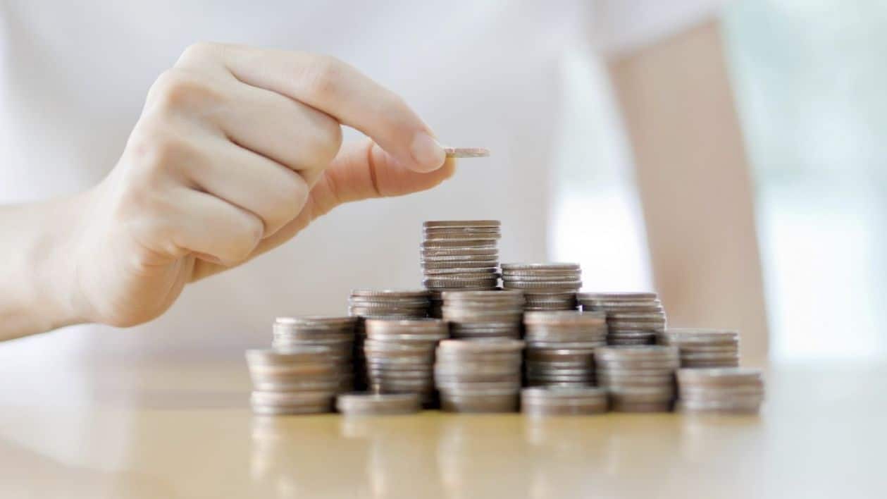En hånd legger mynter oppå hverandre