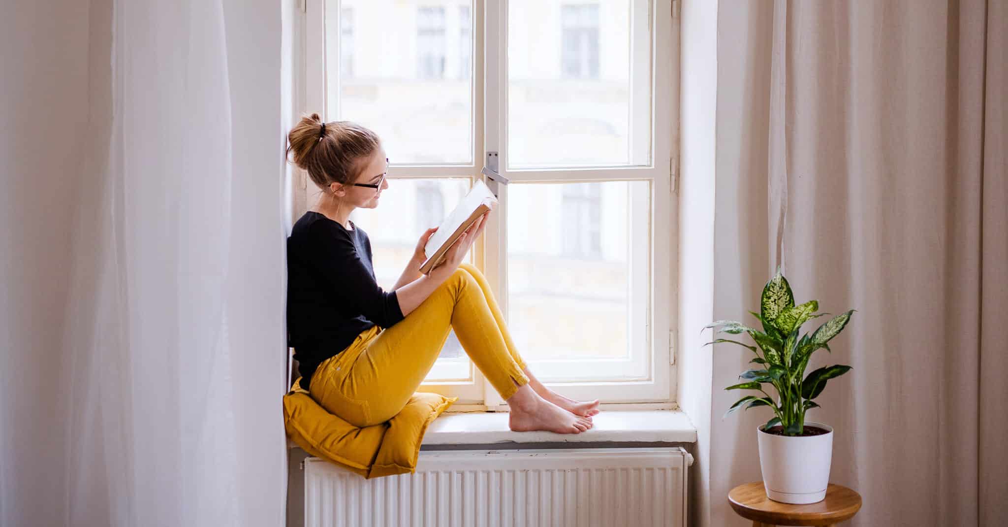 Kvinne leser en bok sittende i en vinduskarm