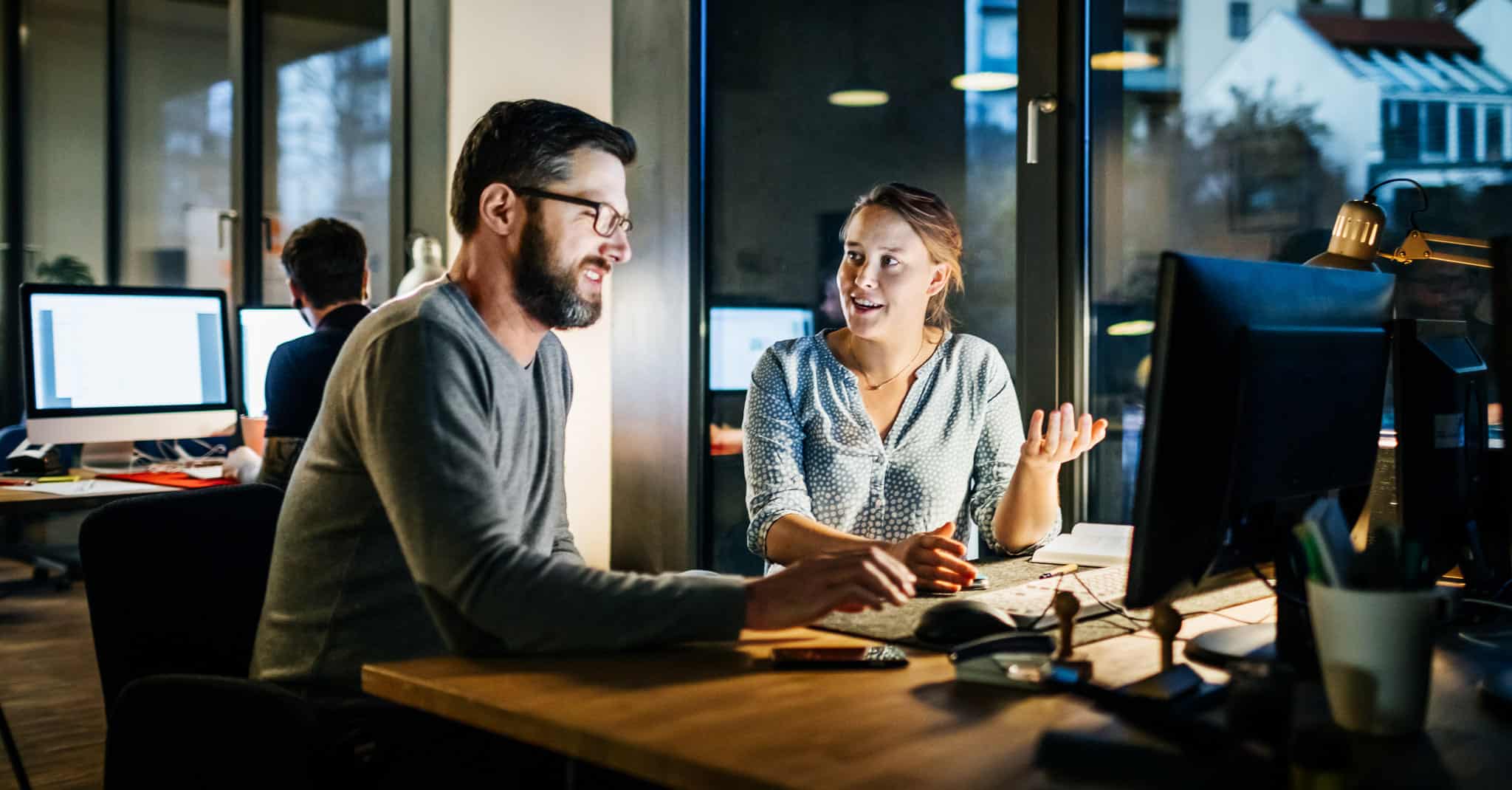 En kvinne prater til en mann foran pcen på et kontor