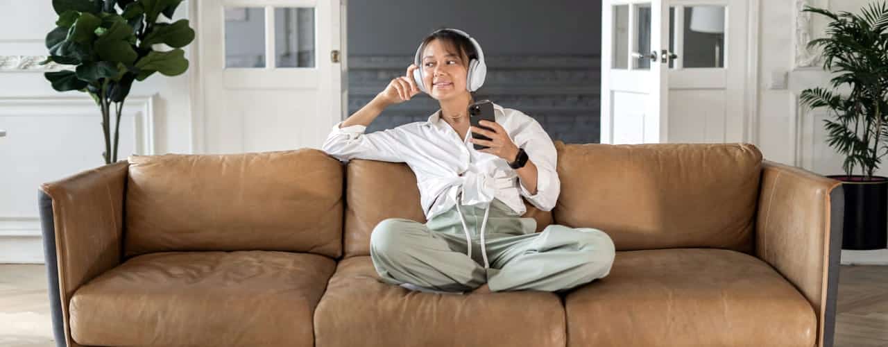 Jent lytter til ebok med hodetelefoner i en sofa og holder en mobil