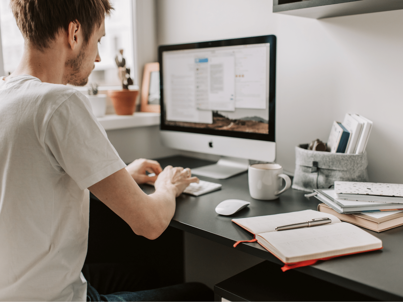 Mann som sitter foran pc med noe dokumenter på siden.